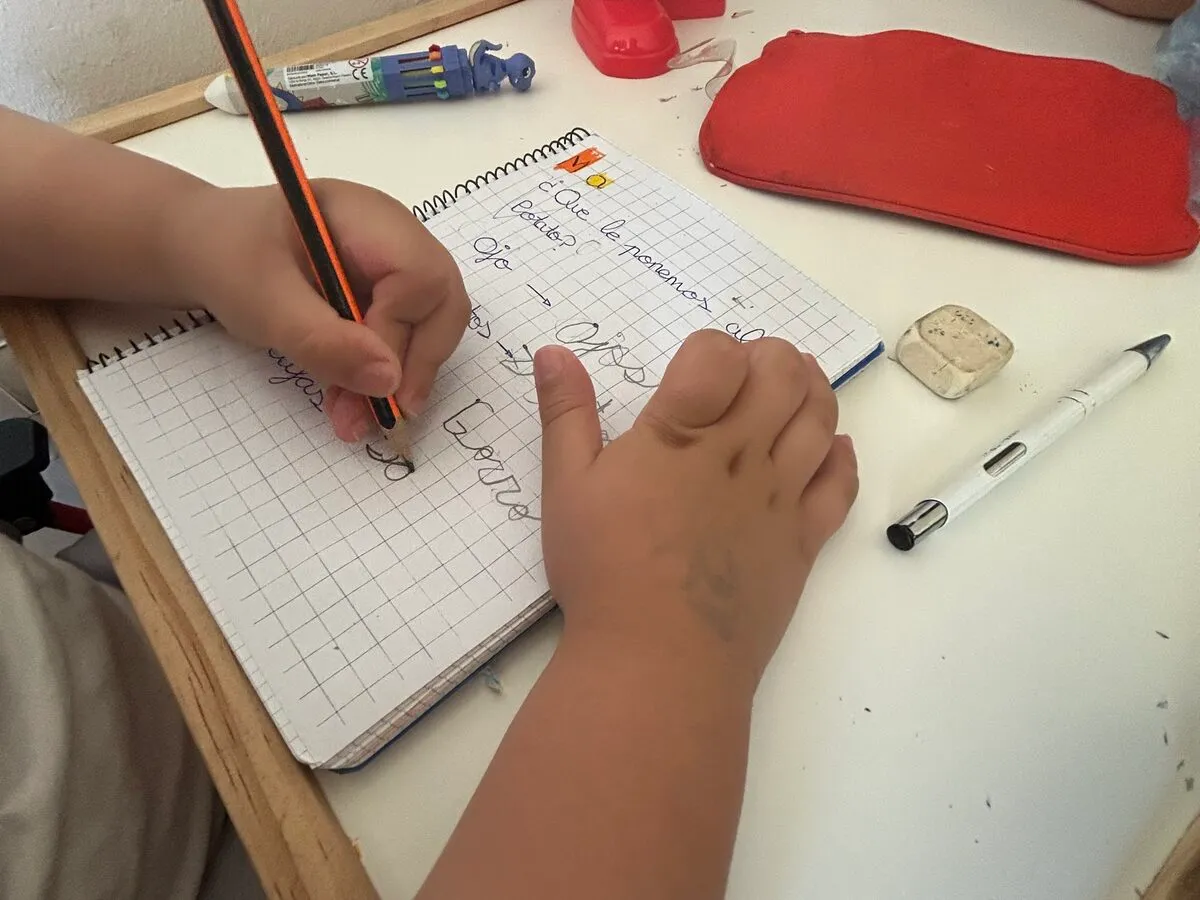 Las manos de un niño escribiendo palabras a lápiz en un cuaderno de cuadrícula